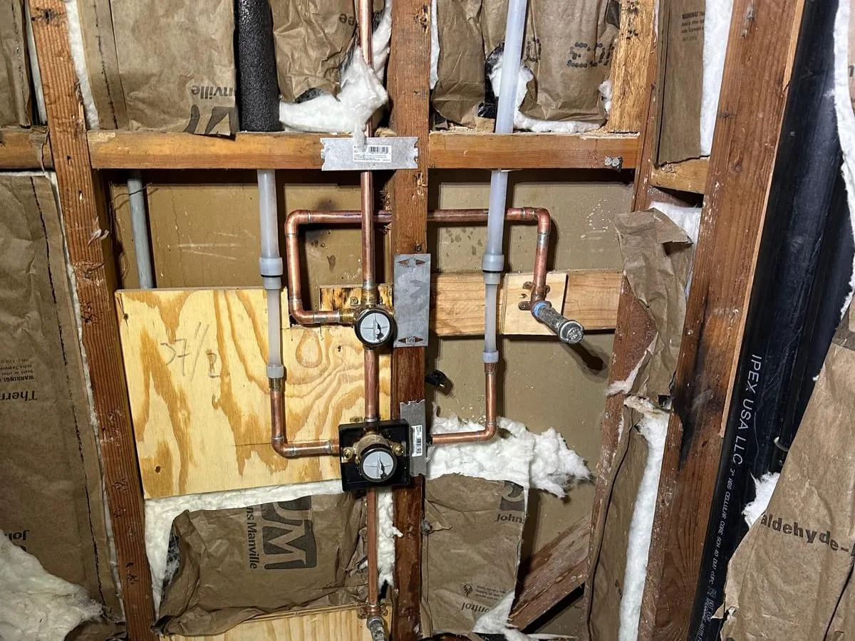 New copper shower piping with a pressure gauge fitted above the valve, in an open wall over a new bathtub